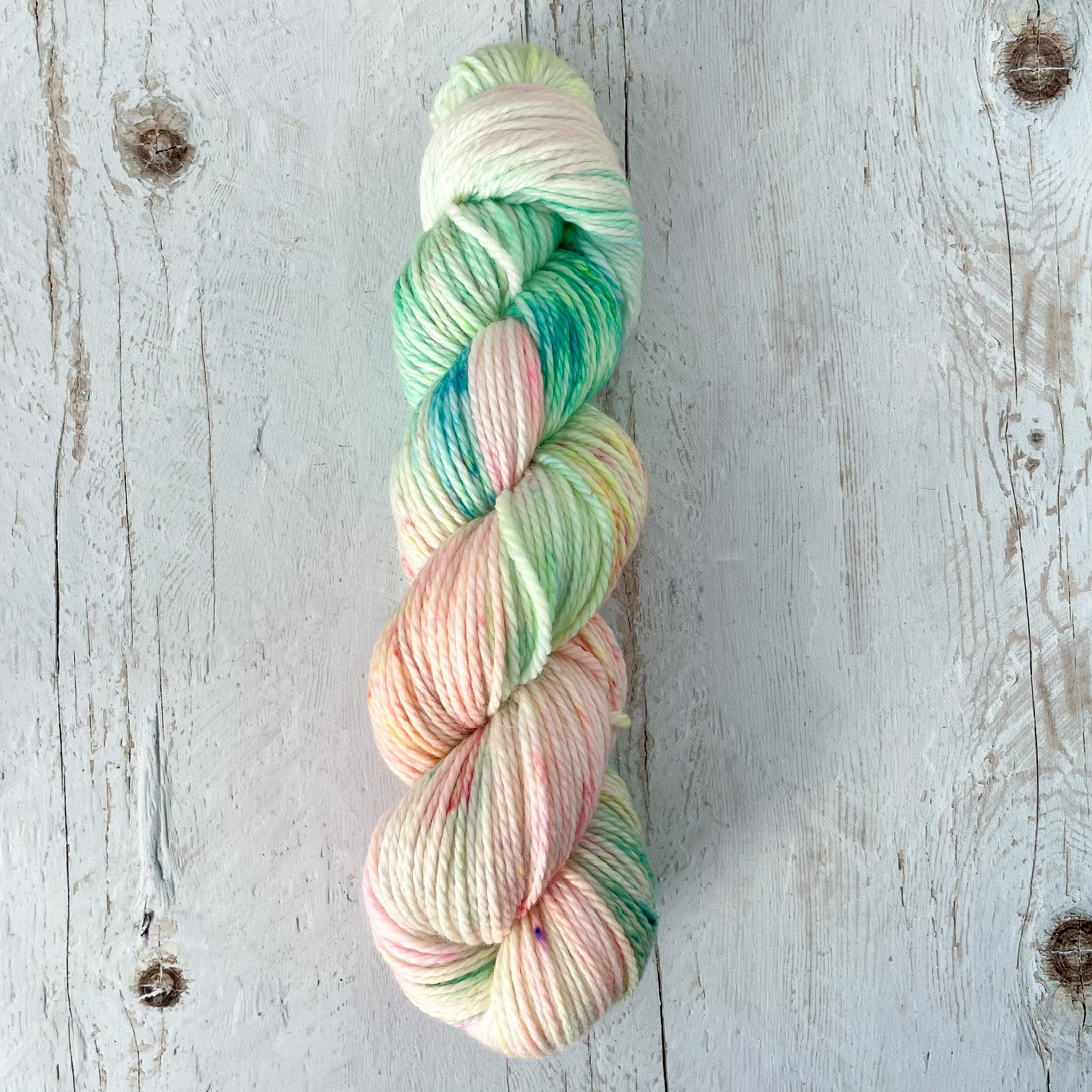 Braided hand dyed merino wool skein of pastel yarn on a wooden background