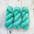 Three skeins of aqua mint hand dyed yarn on a wooden surface