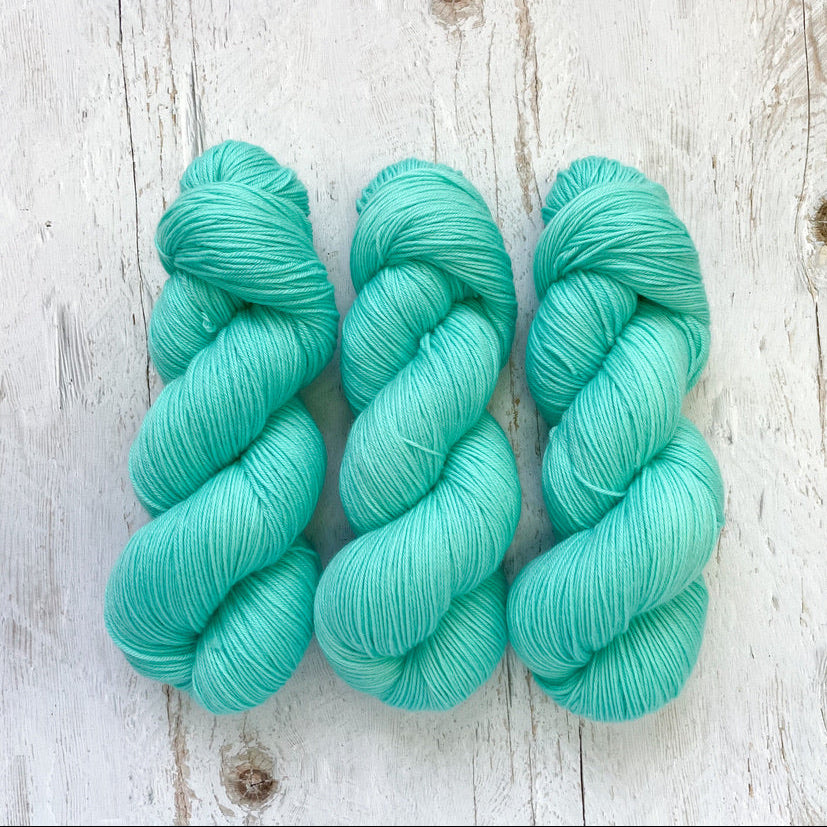 Three skeins of aqua mint hand dyed yarn on a wooden surface