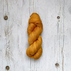 Golden yellow skein of yarn on a textured white wooden surface