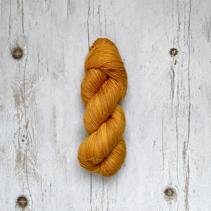 Golden yellow skein of yarn on a textured white wooden surface