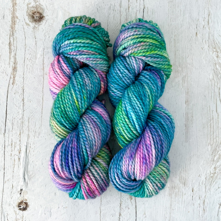 Two skeins of multicolored hand dyed yarn on a light wooden surface