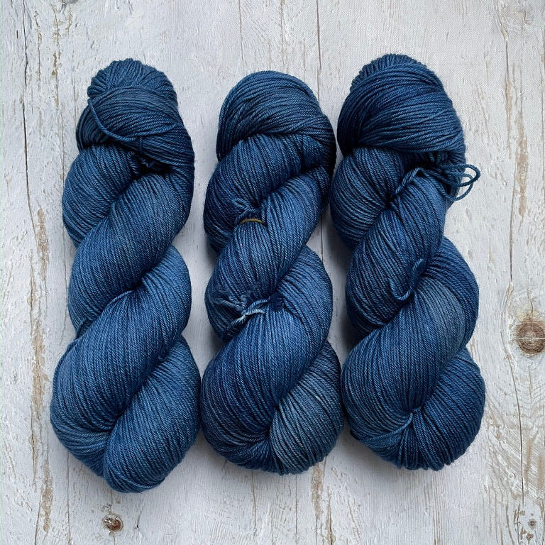 Three skeins of blue yarn on a light wooden surface